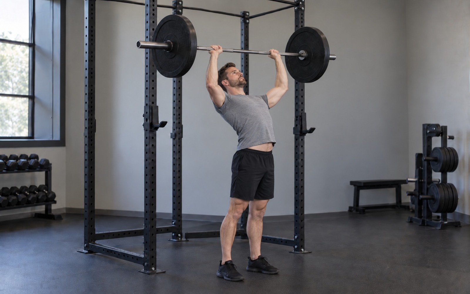 A man performing a standing overhead press with a common mistake: hips pushed forward, lower back arched, ribs flared.