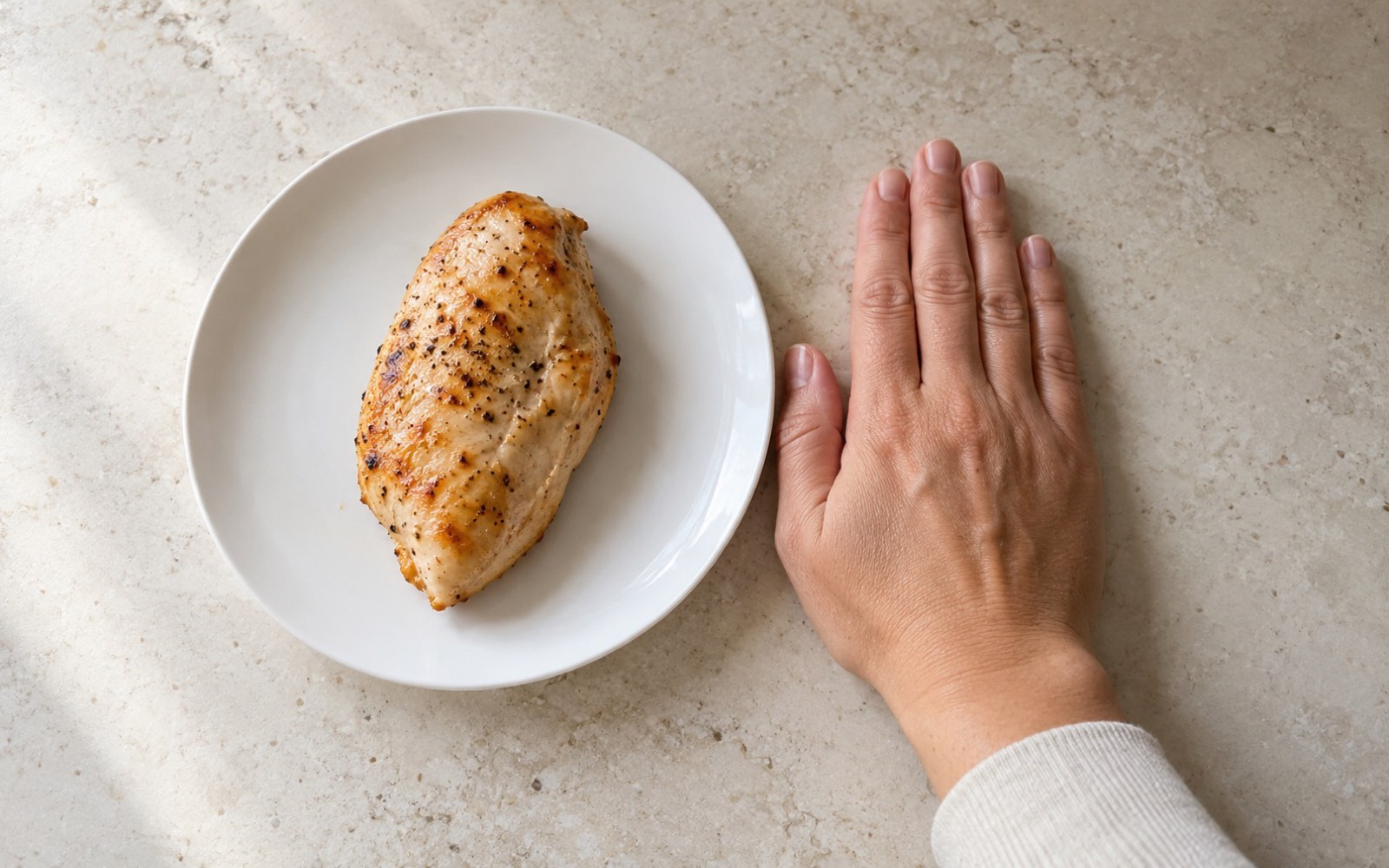 A flat palm lying next to a piece of baked chicken breast of the same size