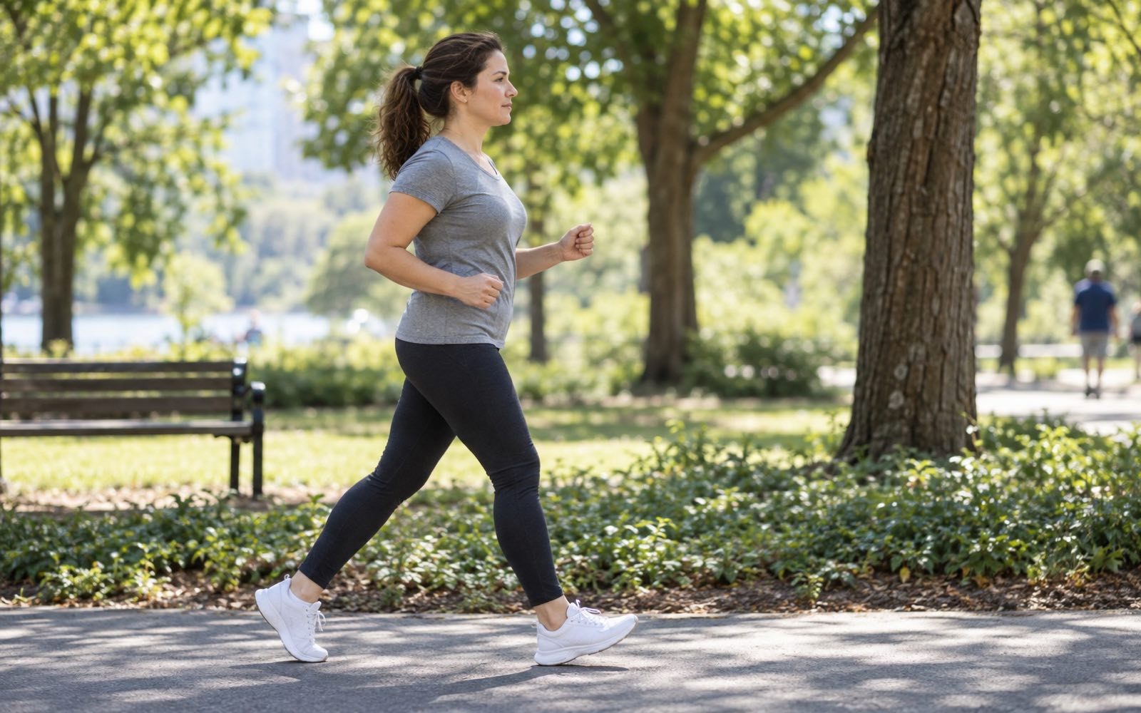 A woman in her mid-thirties walking briskly along a park path during her lunch break, calm and focused expression
