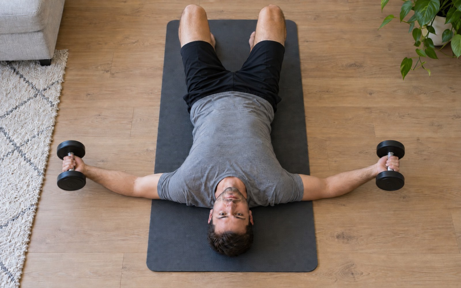 A man performing dumbbell floor flyes at home, top view.