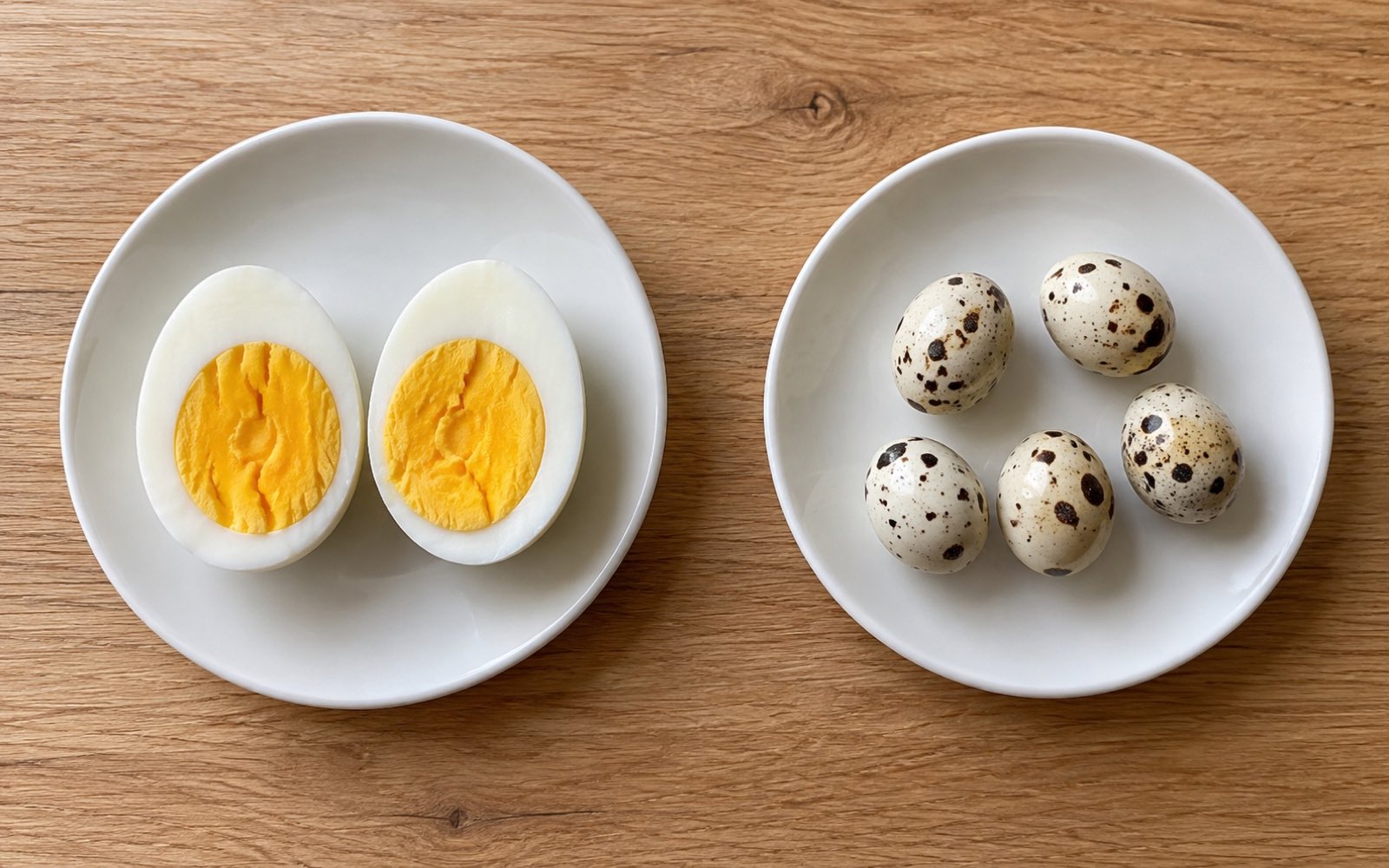 One halved chicken egg on one plate and five quail eggs on another plate beside it
