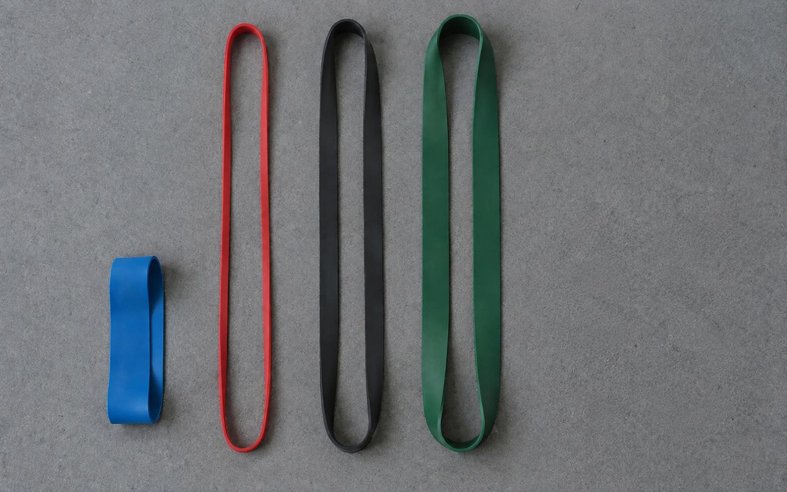Starter set of resistance bands on the floor: a blue mini band and three long loop bands of different widths in red, black and green