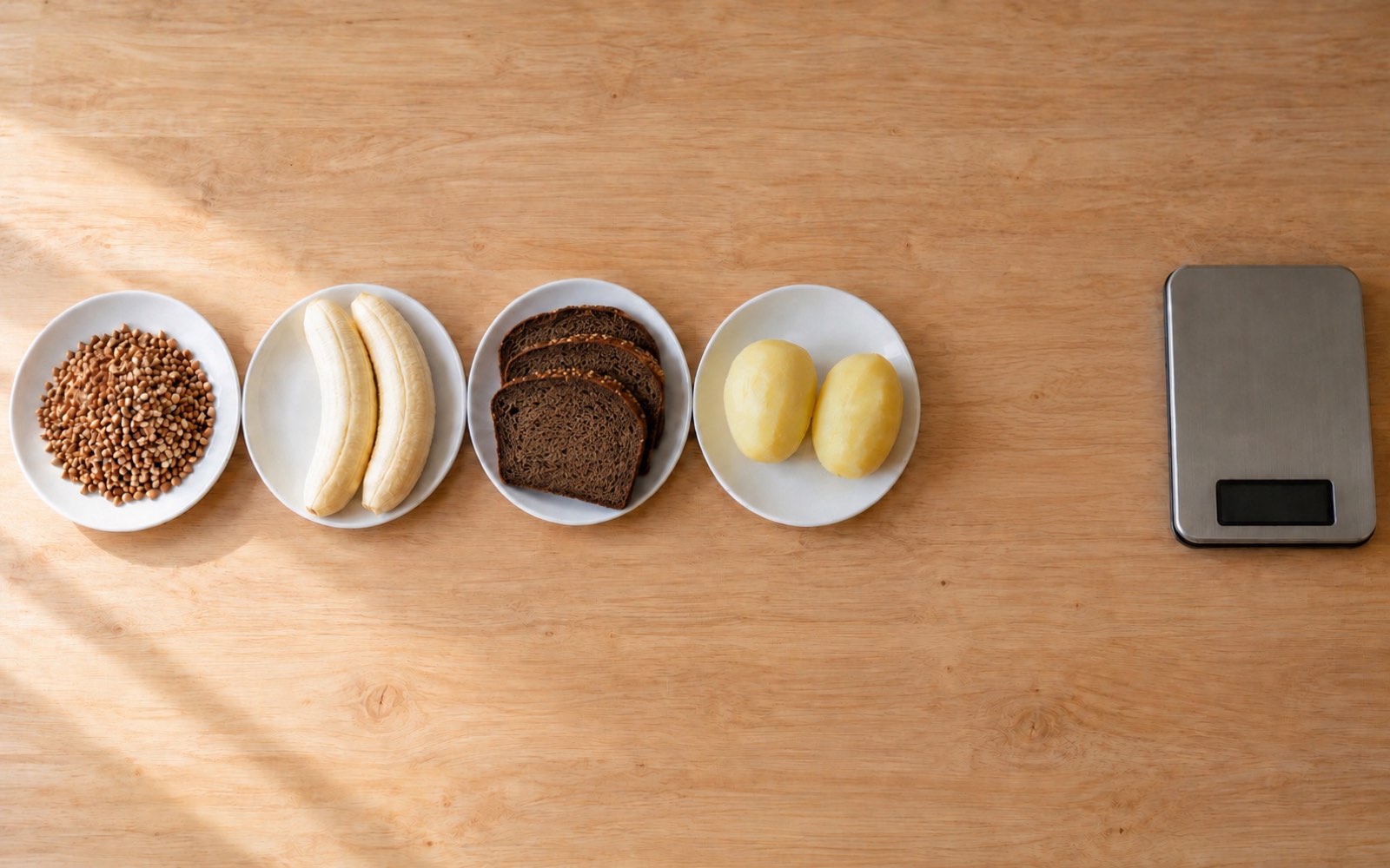 Five plates on a kitchen counter from above — buckwheat, bananas, bread, potatoes and honey, each holding the same amount of carbs
