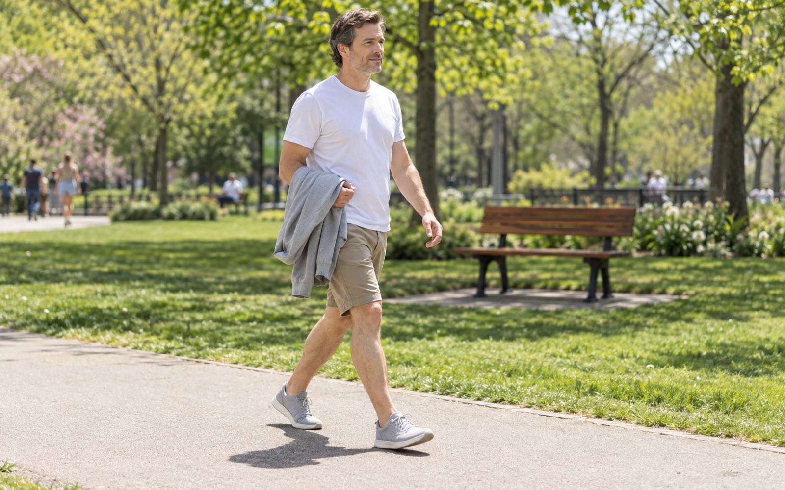 A person walks through a spring park in a t-shirt and shorts, carrying a jacket